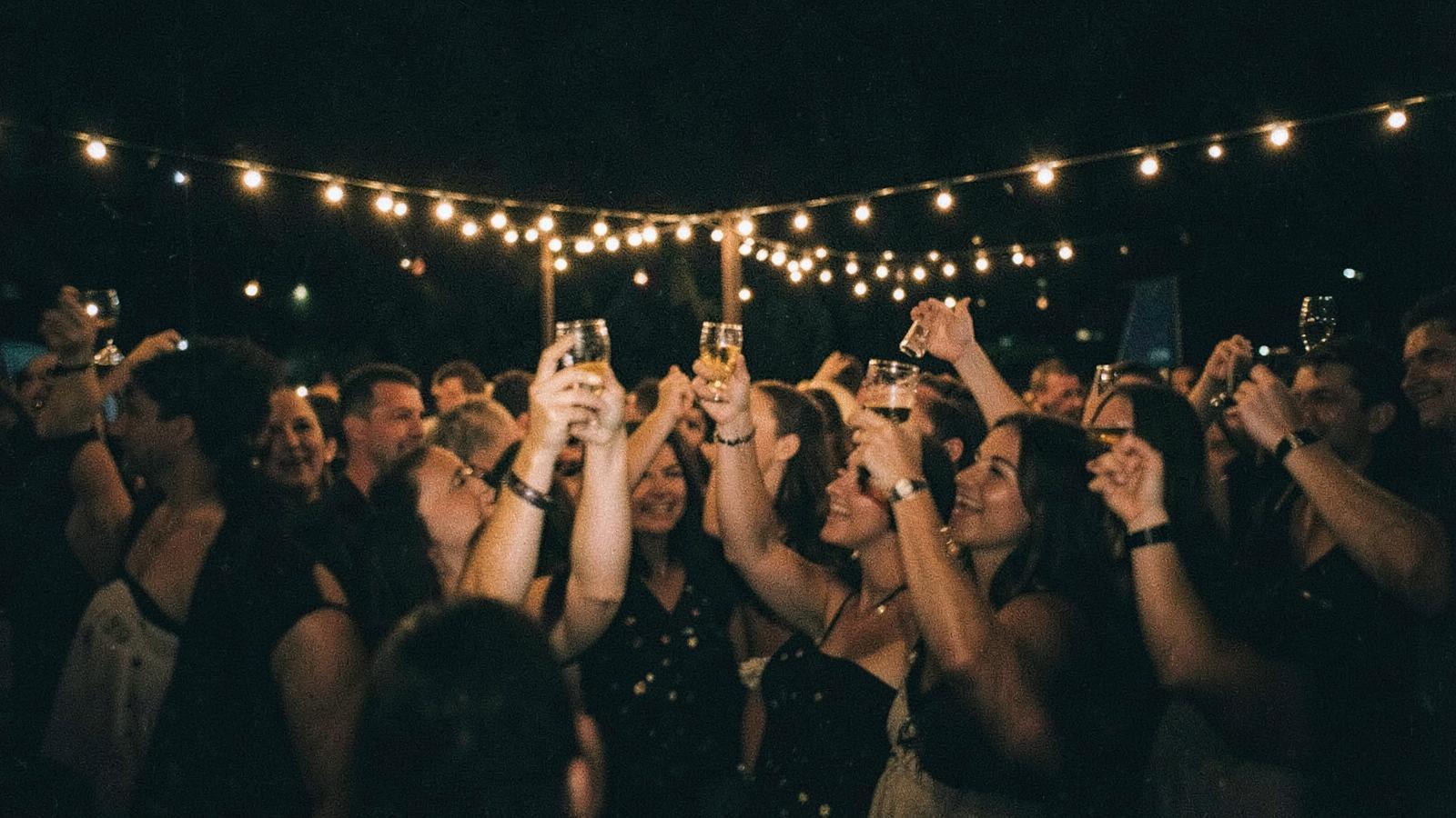 Guests raising glasses under string lights
